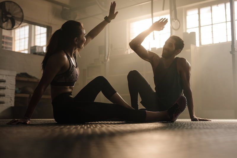 Ein Mann und eine Frau sitzen auf dem Boden in einem Fitnessstudio und unterhalten sich entspannt.
